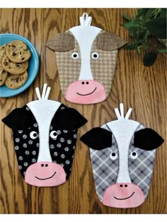 three cow shaped oven mitts sitting on top of a wooden table next to cookies