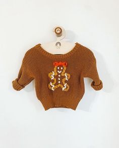 a brown sweater with a bear on it hanging from a white hanger against a wall