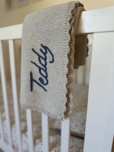 a baby's crib with an embroidered blanket hanging from the rails that have been placed on it