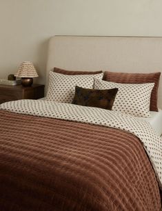 a bed with a brown and white comforter on it next to a night stand