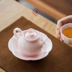 a pink tea pot and saucer sitting on top of a white plate next to a brown place mat