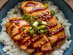 chicken with sesame seeds and sauce on top of rice in a blue bowl, ready to be eaten