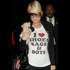 a woman holding a small dog in her right hand and wearing a t - shirt that says i love shoes, bags & boys