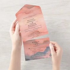 a person holding up two pink and black wedding cards with watercolor designs on them