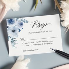 a wedding rsp card with blue flowers on it and a pen next to it