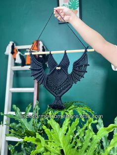 a woman is holding an owl hanging from a plant in front of a green wall