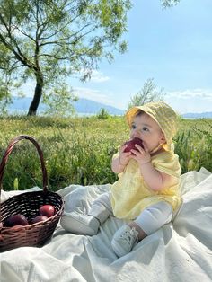 a baby sitting on a blanket with an apple in her hand and a basket next to it