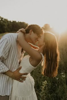 a man and woman kissing in a field at sunset with the sun shining behind them