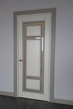 an empty room with a white door and wood flooring on the side, in front of a gray wall