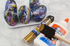 some paint and brushes are sitting on a marble surface next to easter eggs with crosses painted on them