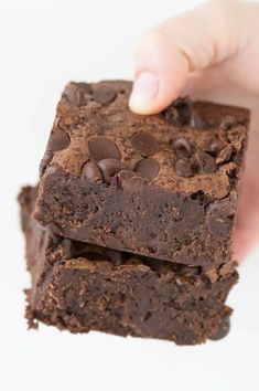 a hand is holding two brownies with chocolate chips