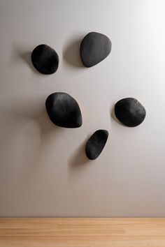 four black rocks arranged in the shape of a face on a white wall next to a wooden floor