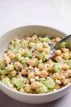 a white bowl filled with chickpeas and cucumber salad next to a spoon