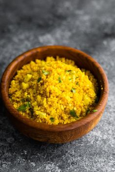 a wooden bowl filled with yellow food on top of a gray counter next to a spoon