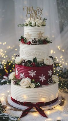 a three tiered wedding cake decorated with white flowers and greenery, on top of snow covered ground