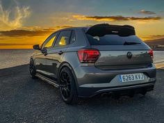 the back end of a gray volkswagen suv parked on top of a beach at sunset