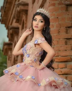 a beautiful young lady wearing a pink dress and tiara posing in front of a brick wall