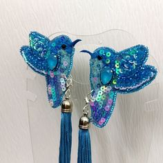 two blue birds with beads and tassels are hanging from hooks on a wall