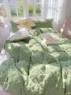 a bed with green comforter and pillows in front of a large flower on the headboard