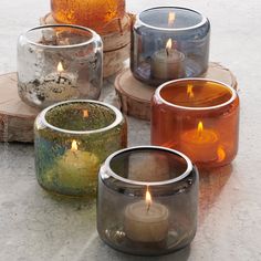 four different colored candles sitting on top of each other in small glass containers with wood slices around them