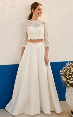 a woman standing next to a wall wearing a white dress and matching crop top with two piece skirt