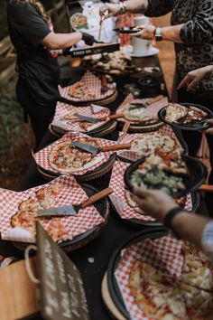 many people are serving themselves pizzas at a buffet table with red and white checkered napkins