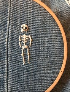 a cross stitched skeleton sitting on top of a piece of denim