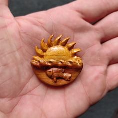 a hand holding a small wooden brooch with a sun on it's face