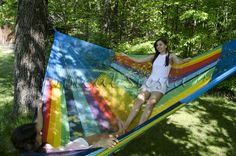 a woman laying in a rainbow colored hammock next to a young man on the grass