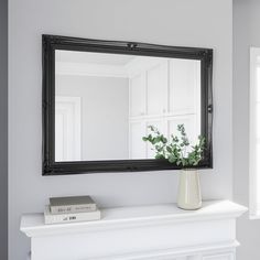 a white fireplace with a mirror on the mantle and a plant in a vase next to it