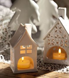 two small white houses with lit candles in front of them on a lace doily