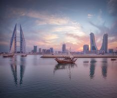 sailboats on the water in front of large cityscape at sunset or dawn