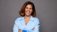 a woman with her arms crossed and smiling at the camera while wearing a blue shirt