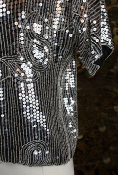 "Alexa, play anything from Abba.... You can dance. You can jive. Have the time of your life in this mesmerizing JLB statement shirt presenting:  ✶Bright dazzling short sleeve dolman silhouette top with bateau neckline  ✶Silver sequins adorned on black 100% Silk throughout  ✶Large paisley shapes scattered throughout embellished design embedded with small pearl beading  ✶Dainty pearl beaded trimming along neckline, sleeve hems, bottom hem, and side seams  ✶Fully lined with shoulder pads. Shell: 100% Silk..Lining: 100% Silk ✩MEASUREMENTS    Size: Medium (Would fit best on a Small or Medium)    Bust: 45\"    Waist: 40\"    Shoulder-Shoulder: 23\"    Sleeve Length: 6\"    Total Length: 22 1/2\" ✶CONDITION: Very Good: used, with very minor flaws, no repairs are necessary. Pearl Beading, Sequin Shirt, Embellished Blouse, Time Of Your Life, Beaded Trim, Sequin Beading, 80s Vintage, Silver Sequin, Vintage Fabrics