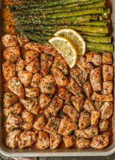 chicken and asparagus in a pan with lemon wedges