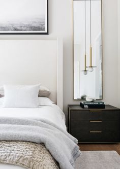 a white bed sitting next to a black dresser with a mirror on top of it