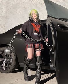 a woman with green hair and black boots is chained to the back of a car