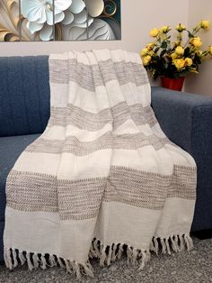 a white and grey blanket sitting on top of a couch next to a vase with yellow flowers