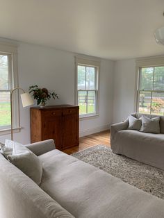 a living room with two couches and a rug on the floor in front of three windows