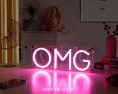 a pink neon sign sitting on top of a table next to a phone and other items