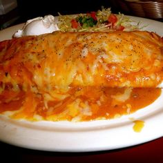 a white plate topped with lasagna covered in cheese and sauce next to a salad