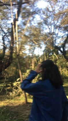 a woman is standing in the woods looking up at something with her hand on her face