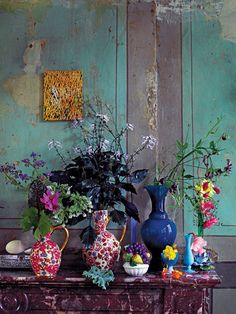 a table topped with vases filled with flowers next to a painting on the wall