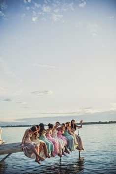 a group of women sitting on top of a wooden pier next to the ocean with their arms in the air