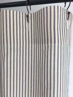 a blue and white striped curtain hanging from a metal rod with two hooks on it