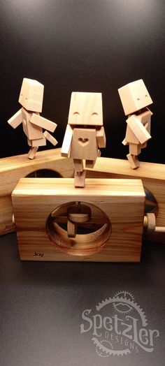 three wooden toy figurines sitting on top of a piece of wood in front of a black background