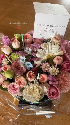 a bouquet of flowers on a table with a card in the middle and a note attached to it