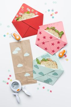 three different colored envelopes with sandwiches in them on a white surface next to scissors and other items