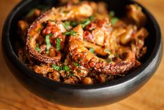 an octopus dish is served in a black bowl on a wooden table with parsley