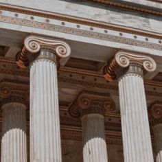 three white pillars with decorative designs on the top and bottom of each column, in front of a building